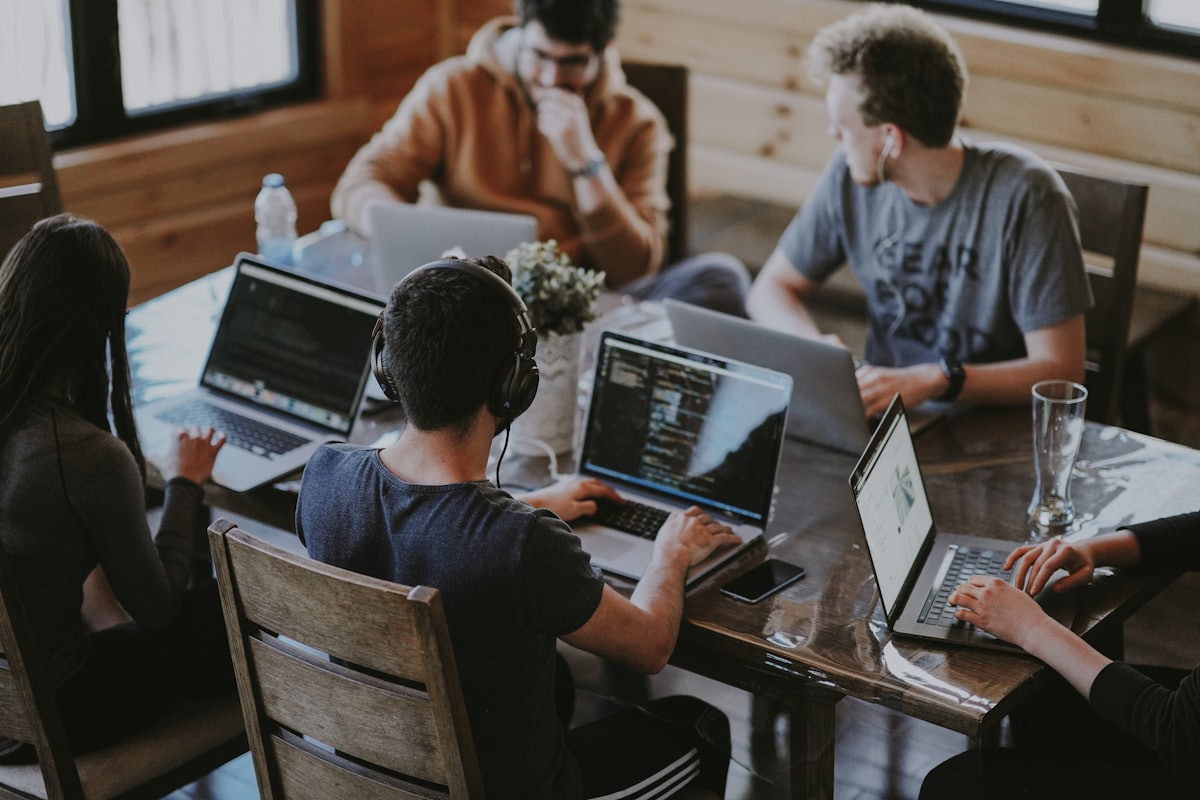 Tim redaksi bekerja bersama di sekitar meja dengan laptop